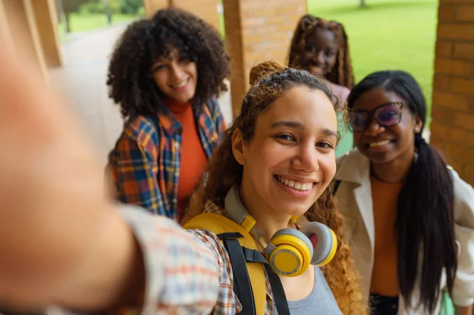 Happy multiracial female students joyfully capturing a selfie on the university campus, celebrating friendship and shared moments outdoors