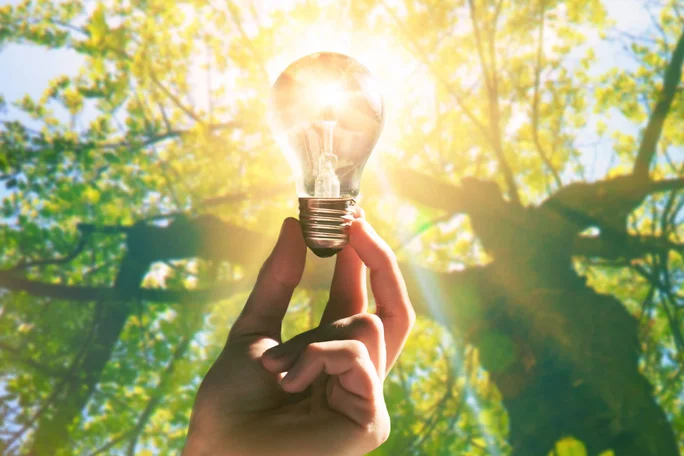 Hand hält Glühbirne gegen Sonnenlicht