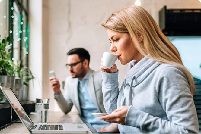 Frau trinkt Kaffee vor einem Laptop und erkundigt sich über Zertifikate von Raiffeisen
