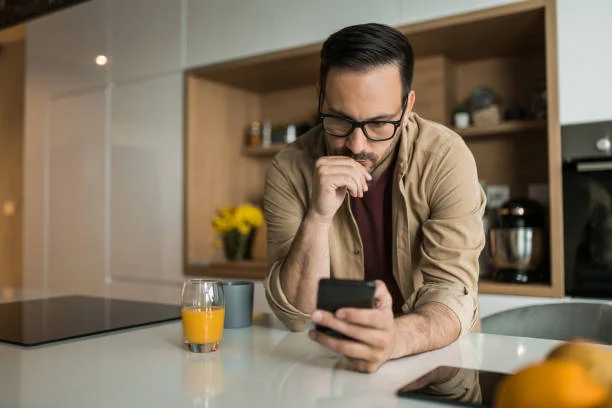 Ein ernster Mann schaut zu Hause auf sein Handy und sinniert.