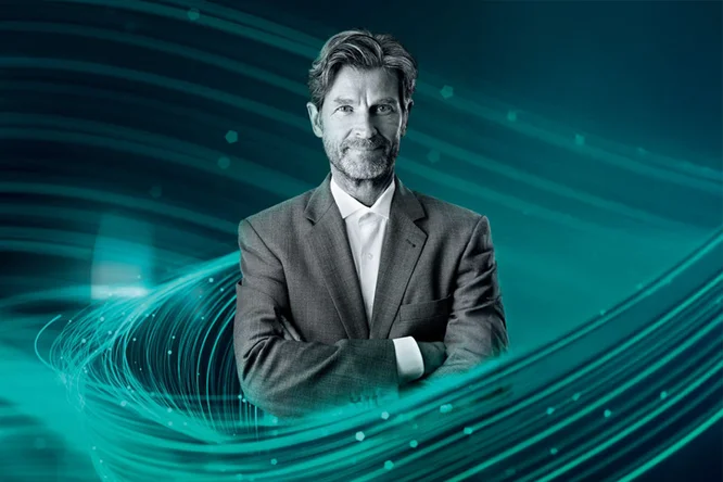 Ein Mann im grauen Anzug steht selbstbewusst mit verschränkten Armen vor einem futuristischen digitalen Hintergrund. Wirbelnde türkisfarbene und blaue Lichtspuren erzeugen einen dynamischen und modernen visuellen Effekt. Das Bild vermittelt Professionalität und Innovation und eignet sich für Unternehmens- oder Technologiethemen.