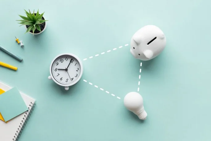 A white piggy bank, an analog clock showing 10:10, and a light bulb are arranged on a pastel blue background. The items are connected with dotted lines, symbolizing ideas of time, savings, and energy. A small potted plant, stationery, and a notebook add to the minimalistic composition.