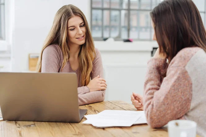 Zwei Frauen unterhalten sich am Schreibtisch.