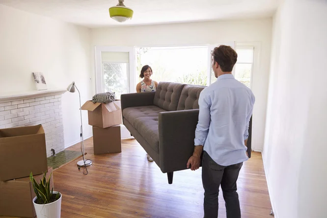 Paar trägt Sofa in helles Wohnzimmer