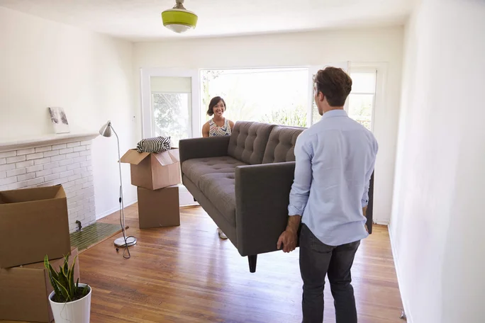 Paar trägt Sofa in helles Wohnzimmer