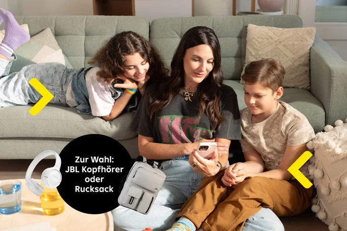 Frau mit Kindern auf dem Sofa  mit dem Text Zur Wahl: JBL Kopfhörer oder Rucksack. Mit Darstellung der Kopfhörer und des Rucksacks