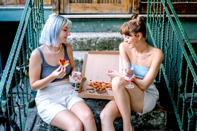 Zwei Frauen sitzen auf der Stiege und essen gemeinsam Pizza