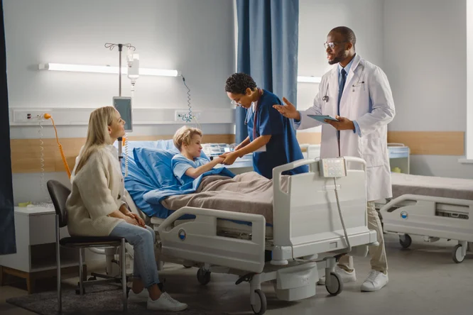 Ein Krankenzimmer mit einem jungen Patienten im Bett, betreut von einer Krankenschwester und einem Arzt im weißen Kittel. Eine sitzende Frau, möglicherweise ein Familienmitglied, beobachtet das Geschehen. Die Umgebung ist mit medizinischen Geräten, Vorhängen und einem sauberen, klinischen Ambiente ausgestattet.