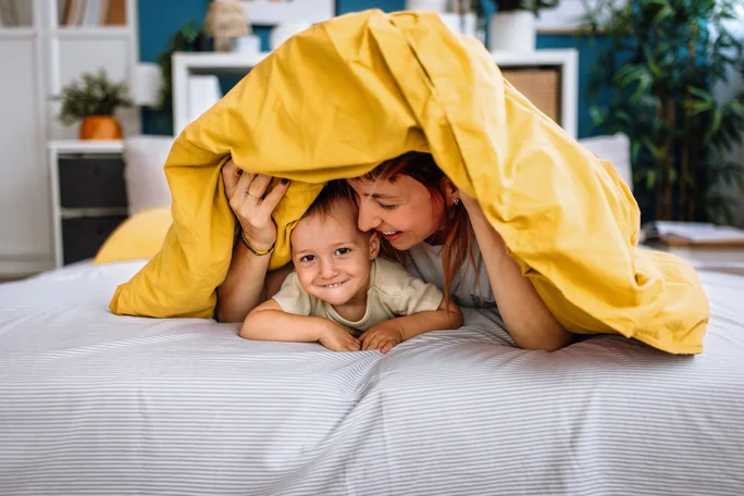 Mutter und Kind spielen und verstecken sich unter einer Decke