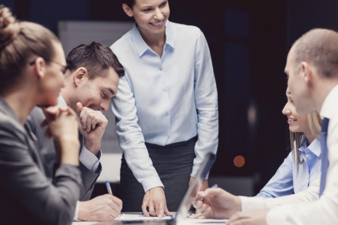 Eine Gruppe von Fachleuten hat sich in einem modernen Büro zu einer Geschäftsbesprechung versammelt. Die zentrale Person steht und deutet auf die Dokumente auf dem Tisch, was auf eine angeregte Diskussion hindeutet. Die Atmosphäre ist geschäftsmäßig geprägt, mit formeller Kleidung und einem Fokus auf Teamarbeit.