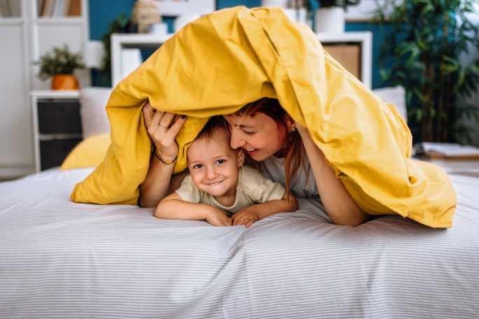 Mutter und Kind spielen und verstecken sich unter einer Decke